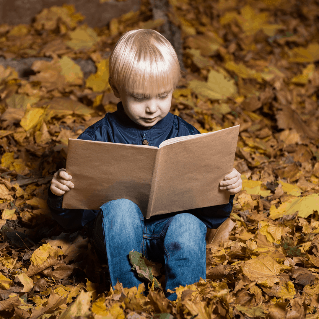 Boy reading sitting in leaves spanish books