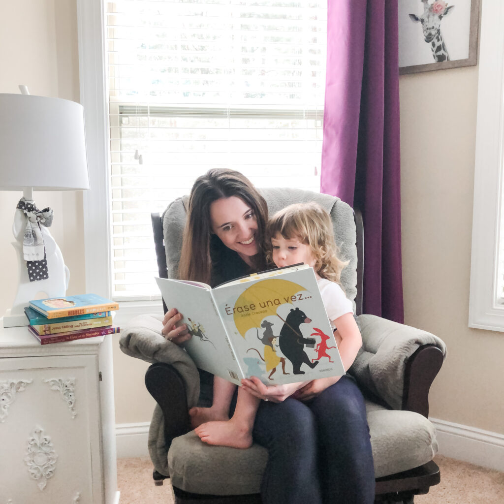 mother reading a Spanish children\'s book to her toddler in a rocking chair
