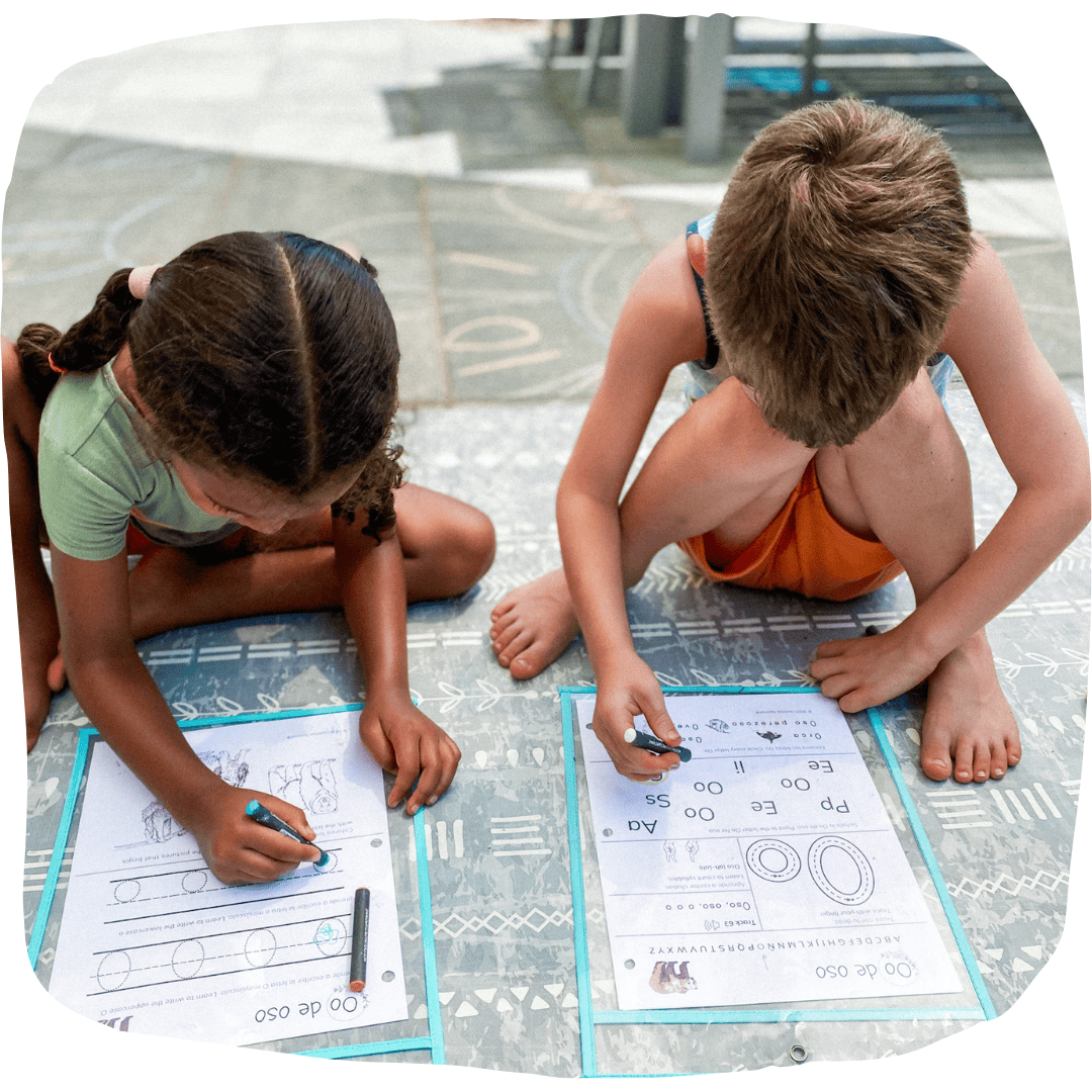 two children completing Spanish printables with crayons