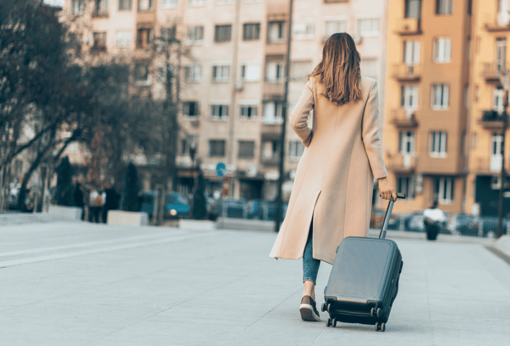 a woman in a long coat is walking her suitcase through a neighborhood